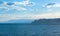 The sea with the silhouette of a jagged rocky shore in the distance with mountains