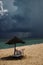 Sea with storm as background, sunbed with umbrella, transparent water