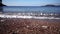 Sea surf rolls on a gravel beach with colorful stones