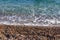 Sea tide on pebble shore of the Mediterranean sea. Waves with white foam on pebble beach