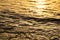 Sea water edge at sunset or sunrise. Texture of golden waves in the rays of setting sun. Copy space