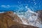 Sea water splashes against the background of the ocean and blue sky. A large ocean wave breaks violently on the rocks