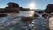 Sea water washes large boulders against the backdrop of mountains