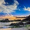 Sea wave breaks about boulders at sunset