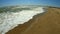 Sea wave with white foam rolls over sandy shore of beach. Top view.