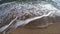 Sea wave with white foam rolls over sandy shore of beach. Top view.