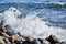 Sea waves break on shingle beach. Small wave rolls onto shore and splash of foam flies in different directions. Beautiful marine