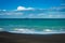 Sea waves breaking on a black sand beach. Distant cargo ship sailing at the horizon