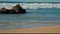 Sea waves crash against the coastal rocks on the sandy beach.