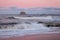 Sea waves and lighthouse on a cliff and on a amazing pink sunset