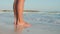 Sea waves rushing to woman legs at beach. Unknown girl standing at seashore.