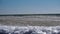 Sea waves with a snowy ice mass run up on the shore, covered with small ice floes. Ice with snow floats on the sea waves near the