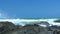 Sea waves splashing on rocky beach on blue sky landscape. Close up water waves breaking on stony coast in ocean. Blue