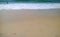 The sea waves splashing on the seashore with footprints along the sandy beach