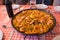 Seafood paella on checkered tablecloth. Delicious seafood. Mediterranean cuisine. Paella pan with king shrimps and wine bottle.
