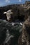 Seagull in the foreground flies over a steep cliff with the rough sea