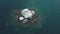 Seagulls flying and nesting on small rock island in the ocean. Aerial view