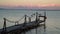 Seagulls sitting on a railing at the pier by the shore at sunset. Swirling water with colourful sunset sky in the background