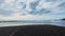 Seagulls soar over the black volcanic sand beach and the beautiful sea.