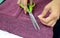 A seamstress cuts a thread on a pink knit fabric with scissors.
