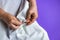 Seamstress`s hands on purple background. Female hands with a needle, thread and thimble. Woman sews light clothes