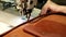 Seamstress sews leather bag in a sewing workshop. Woman operates sewing machine