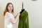 Seamstress standing near mannequin, hanging up cloth and looking at camera