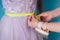 Seamstress tailor dressmaker designer wedding dress measures the volume of the client`s body measuring tape on a blue