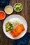 Seared salmon steak with boiled white rice and sliced cucumber on wooden table