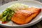 Seared salmon steak with boiled white rice and sliced cucumber on wooden table