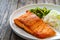 Seared salmon steak with boiled white rice and sliced cucumber on wooden table