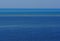 Seascape background with different shades of blue, a stripe of a small emerged sandy island in the middle and a distant ship