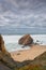 Seascape with beautiful yellow sand beach and majestic rock with a natural cave. Flowers on the cliff of a landscape with an overc