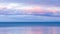 Seascape with blue ocean and pink hazy clouds floating above the horizon