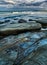 Seascape with bluish rocks and boulders in sea water soft waveâ€™s sky with clouds surfers in the distance