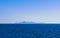 Seascape of calm azure sea and blue sky, no clouds. Sailing boat, hazy distant island, silhouettes of turbine windmills