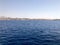 Seascape of the distant beautiful tropical brown stone mountains and different houses, buildings on the shore and blue salt azure