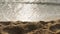 Seascape with focus on fine beach sand in the foreground and blurry waves and ocean water in the background