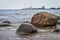 Seascape with stones and boats at the pier in the background.