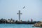 Seascape, view of a big concrete cross on the bay, people walking and birds flying, blue waters and sky, breakwaters, summer seaso