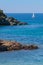 Seashore coastline with cliff and rocks on a mountain slope. Blue sea and a a sailboat in the background. Island of Elba in Italy