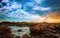 A seaside landscape at sunset with white boulders in foreground and dramatic clouds