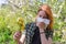 Season allergy to flowering plants pollen. Young woman with dandelion bouquet and paper handkerchief covering her nose in garden.