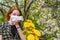 Season allergy to flowering plants pollen. Young woman with dandelion bouquet and paper handkerchief covering her nose in garden.