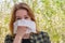 Season allergy to flowering plants pollen. Young woman with paper handkerchief in hand covering her nose in garden. Teen girl