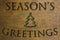 Season`s Greetings banner with a small Christmas tree in a warm green and brown wood tone background.