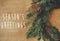 Season`s greetings text sign on christmas rustic wreath flat lay. Creative rural wreath with fir branches, berries, pine cones,