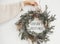 Season`s greetings text sign on christmas rustic wreath in girl hand. Creative rural  wreath with fir branches, berries, pine