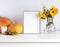 Seasonal autumn fall decorations with photo frame, colorful calendula flowers in a vase and pumpkins on the white chest of drawers