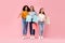 Seasonal sales. Excited three diverse girls holding colorful shopping bags and smiling, posing on pink studio background